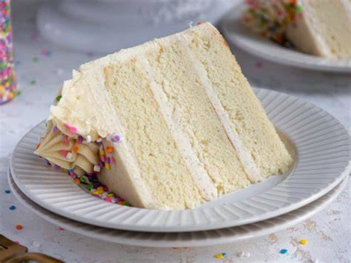 Slice of vanilla cake with colored sprinkles on a white plate.