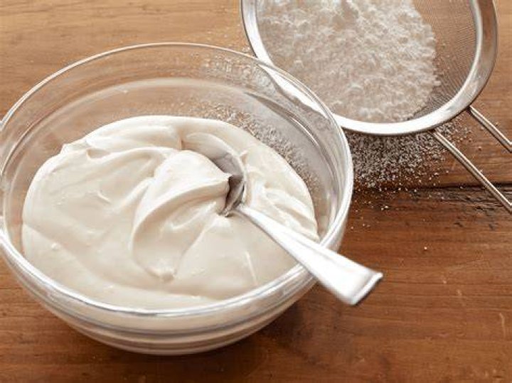 White icing in a glass bowl with a whisk.